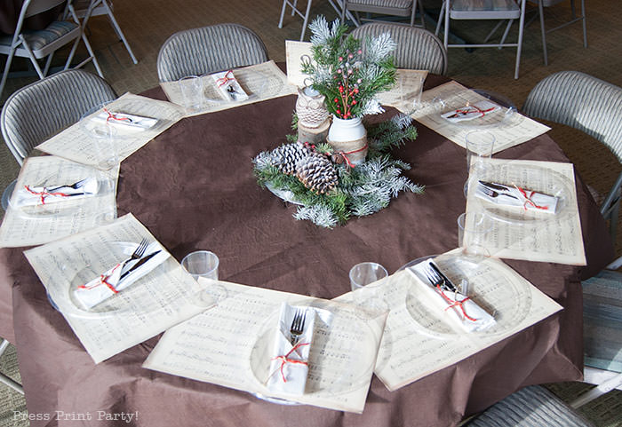 Rustic Christmas table centerpiece with greenery, rustic owl, white mason jar, pinecones, and berries. With a free music sheet table number printable download. With a brown tablecloth and music sheet place mats. Easy and cheap. by Press Print Party!