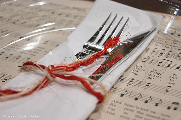 Table setting in white napkin with rafia. Rustic Christmas table centerpiece with greenery, rustic owl, white mason jar, pinecones, and berries. With a free music sheet table number printable download. With a brown tablecloth and music sheet place mats. Easy and cheap. by Press Print Party!