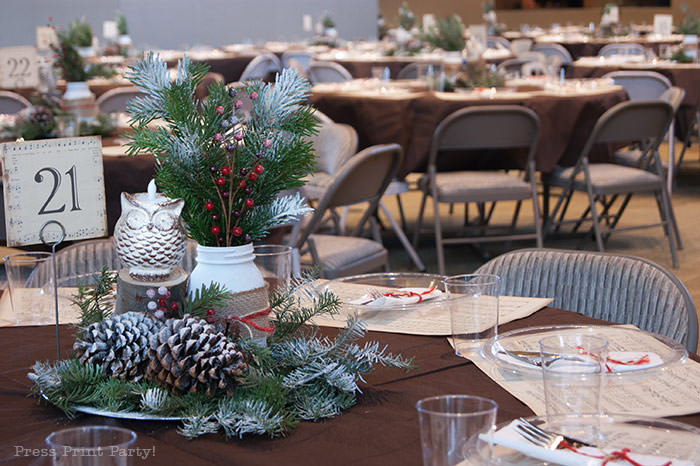 Rustic Christmas table centerpiece with greenery, rustic owl, white mason jar, pinecones, and berries. With a free music sheet table number printable download. With a brown tablecloth and music sheet place mats. Easy and cheap. by Press Print Party!