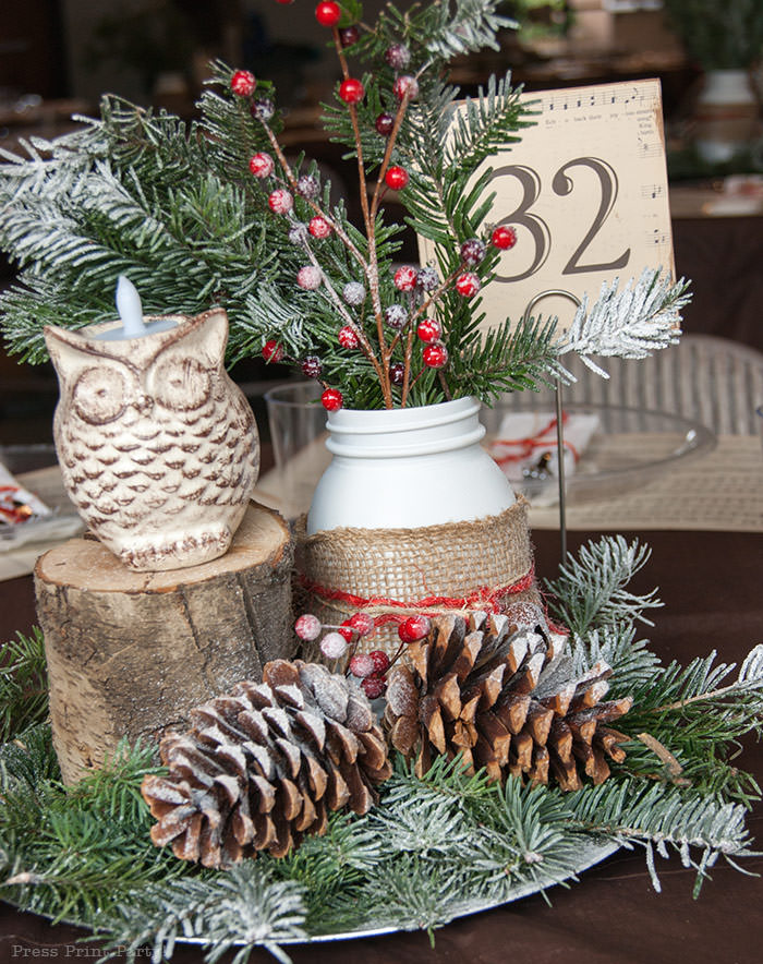 Rustic Christmas table centerpiece with greenery, rustic owl, white mason jar, pinecones, and berries. With a free music sheet table number printable download. With a brown tablecloth and music sheet place mats. Easy and cheap. by Press Print Party!