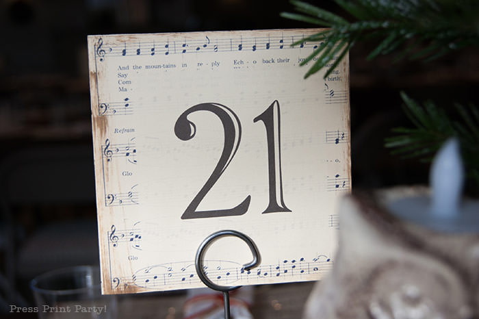 table number with music sheet. Rustic Christmas table centerpiece with greenery, rustic owl, white mason jar, pinecones, and berries. With a free music sheet table number printable download. With a brown tablecloth and music sheet place mats. Easy and cheap. by Press Print Party!