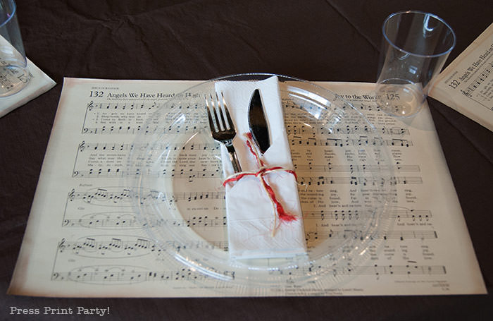 Table setting in white napkin with rafia. Rustic Christmas table centerpiece with greenery, rustic owl, white mason jar, pinecones, and berries. With a free music sheet table number printable download. With a brown tablecloth and music sheet place mats. Easy and cheap. by Press Print Party!