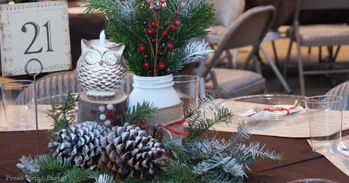 Rustic Christmas table centerpiece with greenery, rustic owl, white mason jar, pinecones, and berries. With a free music sheet table number printable download. With a brown tablecloth and music sheet place mats. Easy and cheap. by Press Print Party!