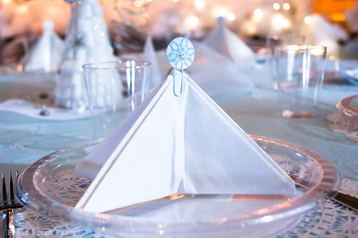 table setting with a tree napkin and a snowflake topper on a lace doily white For Christmas table decor ideas blue and silver winter wonderland decorations. Christmas tablescape for large event christmas party, diy holiday table setting. by Press Print Party!