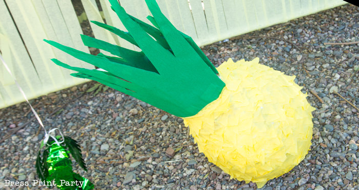 Pineapple pinata on the ground with a yellow streamer body and green top. Press Print Party!