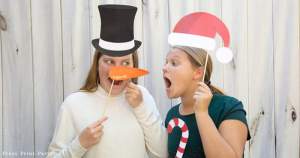 2 girls with Christmas photo booth props printables, one with a snowman hat and carrot nose, the other with santa hat and candy cane - Press Print Party!