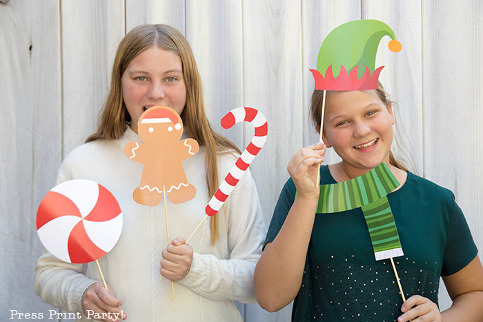 2 girls with Christmas photo booth props. one with a gingerbread man and candy cane, the other with elf hat and scarf - Press Print Party!