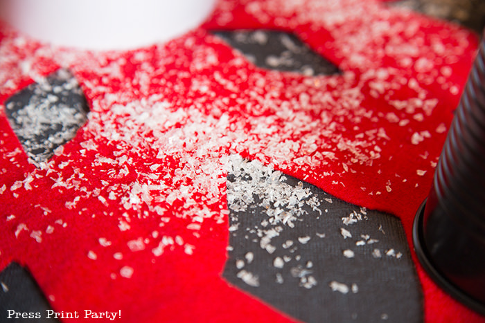 close up of red felt snowflake table centerpiece with snow on black tablecloth - Press Print Party!