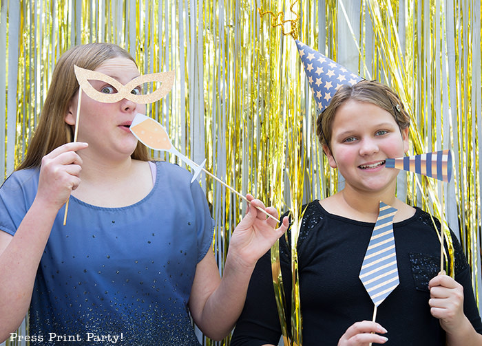 2 girls having fun with new year's eve photo booth props. party hat, noise maker, champagne glass, mask - Press Print Party!