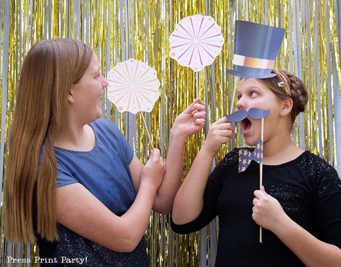 2 girls having fun with new year's eve photo booth props. hat, mustache and fireworks- Press Print Party!