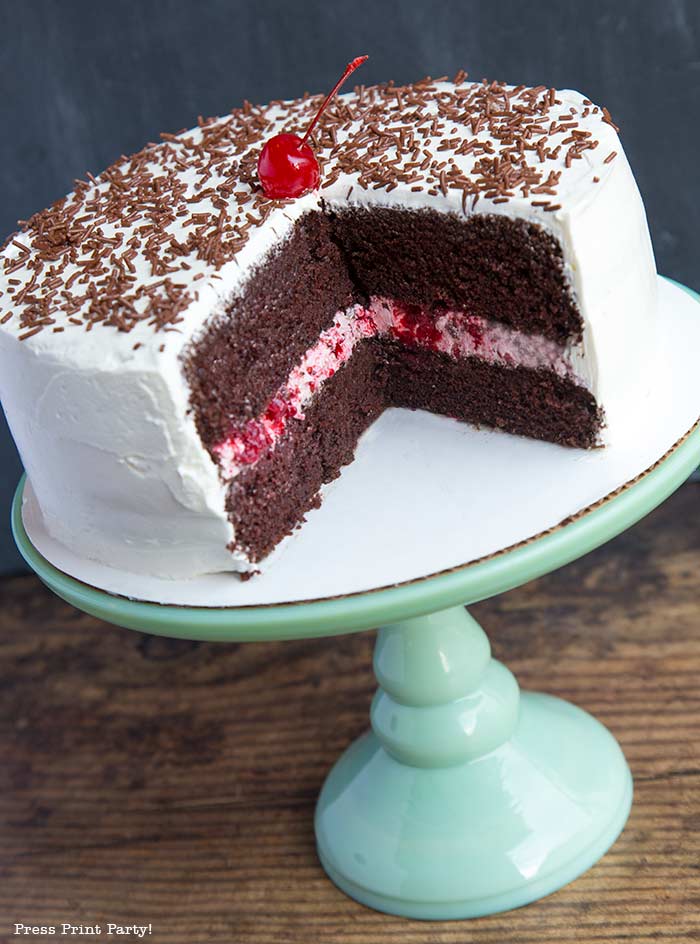 Moist chocolate cake with white frosting and berry filling on a green pedestal with a cherry on top - Press Print Party!