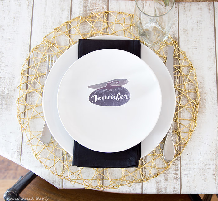 Golden Farmhouse Decorations for Thanksgiving Table. Get inspired with Thanksgiving table decor ideas. White wooden walls with gilded wreath and gold chargers, white plates, black pumpkin place cards, black lantern, golden pumpkins, votives, decorations for thanksgiving table, farmhouse decor ideas, Friendsgiving ideas, thanksgiving table decor, Thanksgiving table setting - tablescape. Press Print Party!