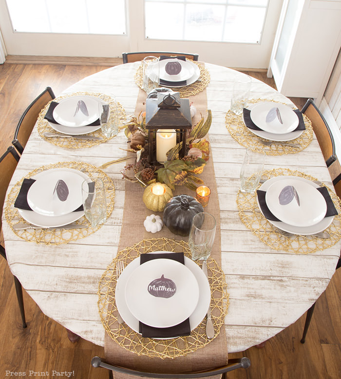 Golden Farmhouse Decorations for Thanksgiving Table. Get inspired with Thanksgiving table decor ideas. White wooden walls with gilded wreath and gold chargers, white plates, black pumpkin place cards, black lantern, golden pumpkins, votives, decorations for thanksgiving table, farmhouse decor ideas, Friendsgiving ideas, thanksgiving table decor, Thanksgiving table setting - tablescape. Press Print Party!