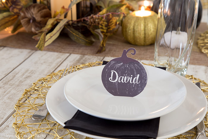 Golden Farmhouse Decorations for Thanksgiving Table. Get inspired with Thanksgiving table decor ideas. White wooden walls with gilded wreath and gold chargers, white plates, black pumpkin place cards, black lantern, golden pumpkins, votives, decorations for thanksgiving table, farmhouse decor ideas, Friendsgiving ideas, thanksgiving table decor, Thanksgiving table setting - tablescape. Press Print Party!