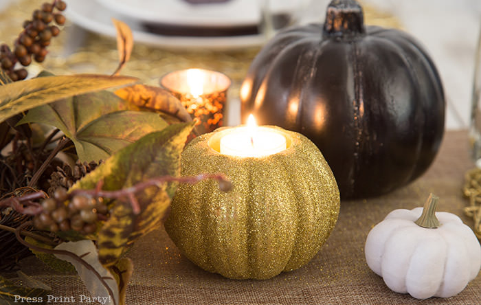 Golden Farmhouse Decorations for Thanksgiving Table. Get inspired with Thanksgiving table decor ideas. White wooden walls with gilded wreath and gold chargers, white plates, black pumpkin place cards, black lantern, golden pumpkins, votives, decorations for thanksgiving table, farmhouse decor ideas, Friendsgiving ideas, thanksgiving table decor, Thanksgiving table setting - tablescape. Press Print Party!