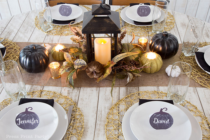 Golden Farmhouse Decorations for Thanksgiving Table. Get inspired with Thanksgiving table decor ideas. White wooden walls with gilded wreath and gold chargers, white plates, black pumpkin place cards, black lantern, golden pumpkins, votives, decorations for thanksgiving table, farmhouse decor ideas, Friendsgiving ideas, thanksgiving table decor, Thanksgiving table setting - tablescape. Press Print Party!