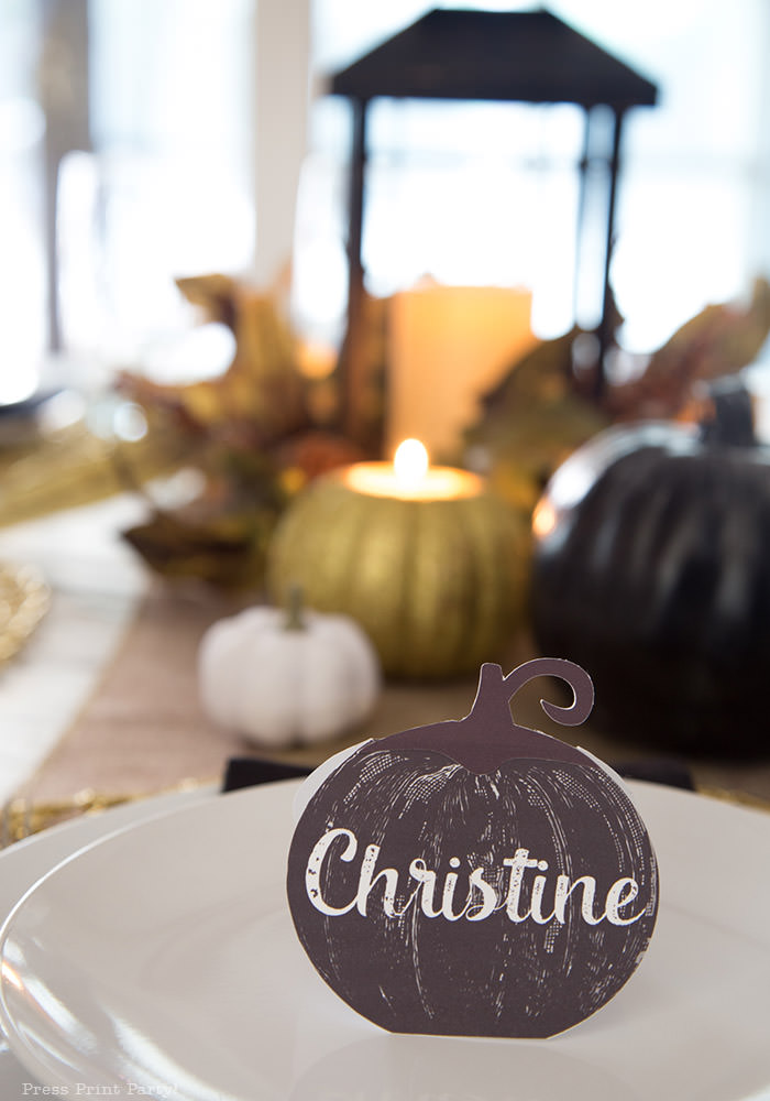 Golden Farmhouse Decorations for Thanksgiving Table. Get inspired with Thanksgiving table decor ideas. White wooden walls with gilded wreath and gold chargers, white plates, black pumpkin place cards, black lantern, golden pumpkins, votives, decorations for thanksgiving table, farmhouse decor ideas, Friendsgiving ideas, thanksgiving table decor, Thanksgiving table setting - tablescape. Press Print Party!