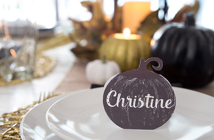 Golden Farmhouse Decorations for Thanksgiving Table. Get inspired with Thanksgiving table decor ideas. White wooden walls with gilded wreath and gold chargers, white plates, black pumpkin place cards, black lantern, golden pumpkins, votives, decorations for thanksgiving table, farmhouse decor ideas, Friendsgiving ideas, thanksgiving table decor, Thanksgiving table setting - tablescape. Press Print Party!