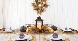 Golden Farmhouse Decorations for Thanksgiving Table. Get inspired with Thanksgiving table decor ideas. White wooden walls with gilded wreath and gold chargers, white plates, black pumpkin place cards, black lantern, golden pumpkins, votives, decorations for thanksgiving table, farmhouse decor ideas, Friendsgiving ideas, thanksgiving table decor, Thanksgiving table setting - tablescape. Press Print Party!