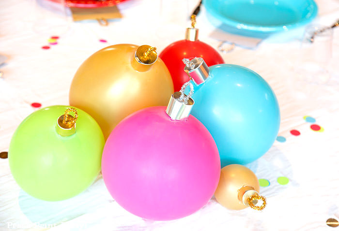 close up of large ornament christmas centerpiece with ballons. Balloons with ornament toppers in green, gold, blue, red and hot pink. Christmas tablescape balloon centerpiece decoration with large ornament balloons and plates that look like ornaments. Very cheery and bright. Fun and creative for your Christmas party. Simple Christmas balloon decor ideas diy. Press Print Party!