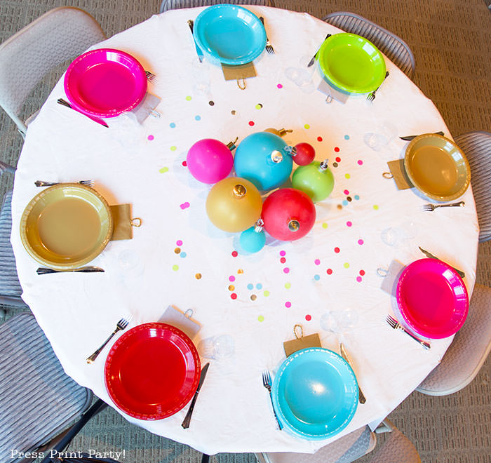 over the top shot of a Christmas party table round. Christmas tablescape balloon centerpiece decoration with large ornament balloons and plates that look like ornaments. Very cheery and bright. Fun and creative for your Christmas party. Simple Christmas balloon decor ideas diy. Press Print Party!