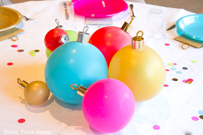 close up of large ornament christmas centerpiece with ballons. Balloons with ornament toppers in green, gold, blue, red and hot pink. Christmas tablescape balloon centerpiece decoration with large ornament balloons and plates that look like ornaments. Very cheery and bright. Fun and creative for your Christmas party. Simple Christmas balloon decor ideas diy. Press Print Party!