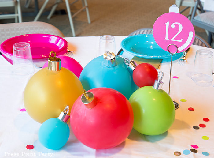 close up of large ornament christmas centerpiece with ballons. Balloons with ornament toppers in green, gold, blue, red and hot pink. Christmas tablescape balloon centerpiece decoration with large ornament balloons and plates that look like ornaments. Very cheery and bright. Fun and creative for your Christmas party. Simple Christmas balloon decor ideas diy. Press Print Party!