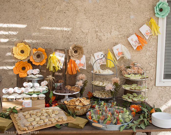 Woodland baby shower snack table. food table with banner and tassels and paper flowers on a pallet backdrop.