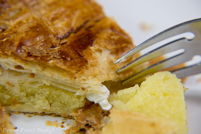 Authentic galette des rois recipe - Piece on a plate with a feve and a fork.French kings cake pastry with almond paste. French tradition, French style kings cake. easy to make with golden crown and feve by Press Print Party!