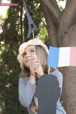 Girl with Paris photo booth props on top of cardboard Eiffel tower with french flag and beret. Press Print Party