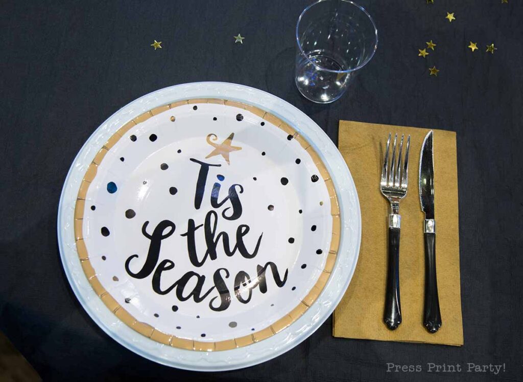 christmas table setup for christmas banquet. Tis the season plates in gold and black with gold napkins and star confetti. Press Print Party!