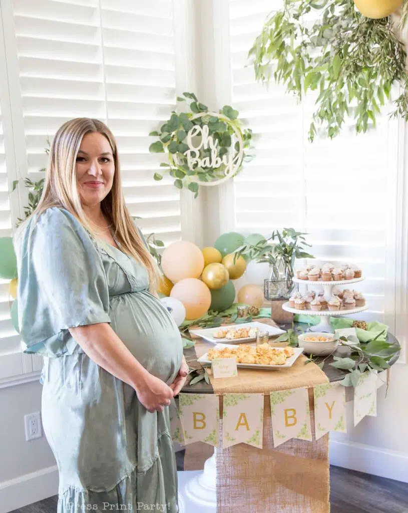 Greenery baby shower decor ideas with printable banner and eucalyptus on table and balloons peach and green and oh baby sign with pregnant woman- Press Print Party!