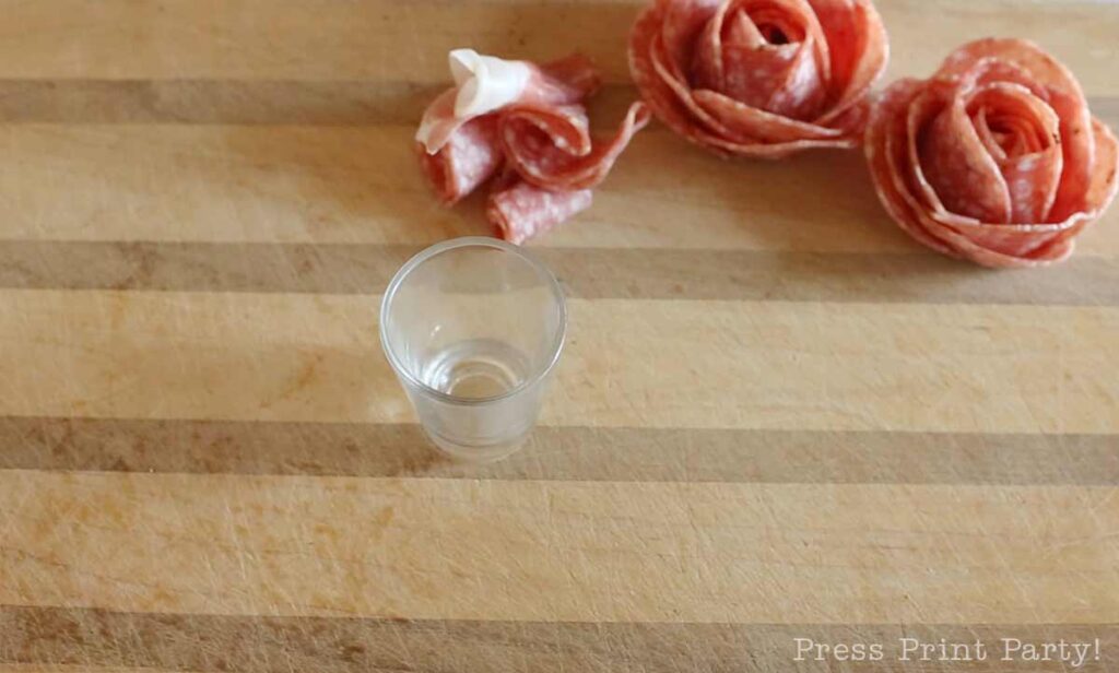 Shot glass on cutting board -how to make a salami rose for your charcuterie board - Press Print Party