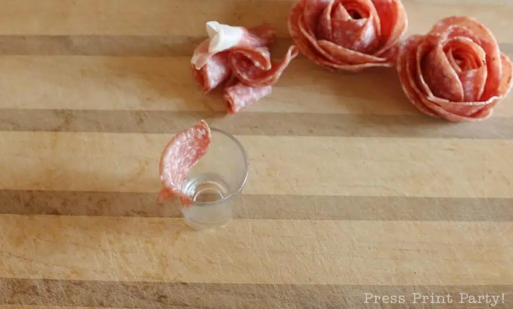 salami slice over shot glass -how to make a salami rose for your charcuterie board - Press Print Party