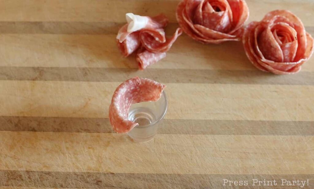 salami slices over shot glass -how to make a salami rose for your charcuterie board - Press Print Party