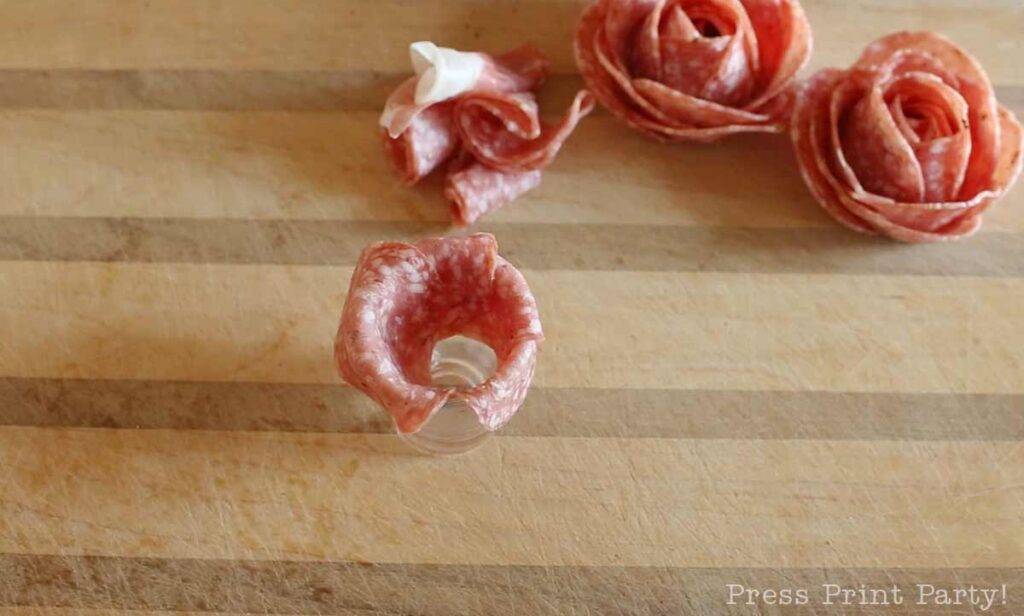 salami slices over shot glass -how to make a salami rose for your charcuterie board - Press Print Party