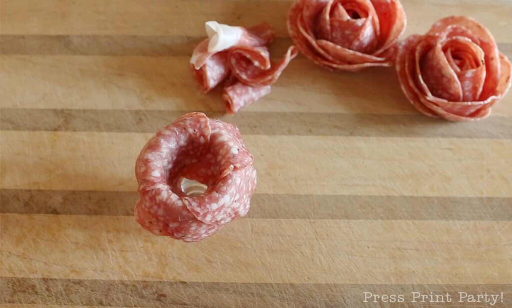 salami slices over shot glass -how to make a salami rose for your charcuterie board - Press Print Party