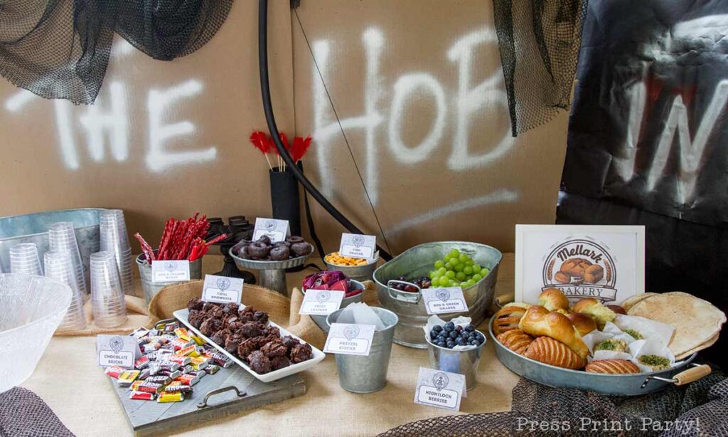 the hob food table with bow and arrow decorations- Our epic hunger games party for teens, hunger games party theme birthday party, food, decorations and games - Press Print Party
