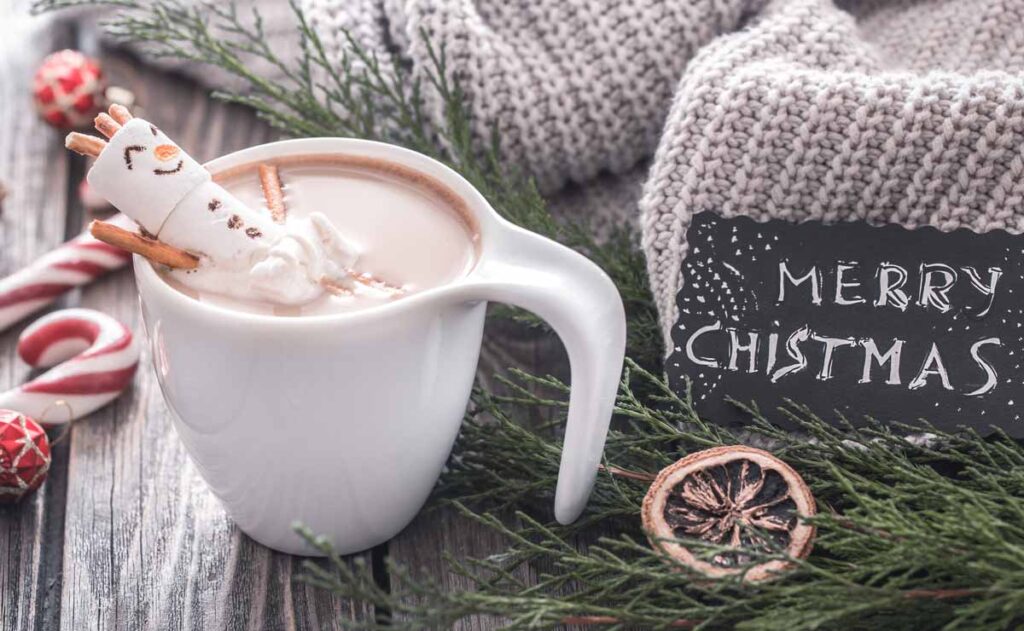 marshmallow snowman in hot chocolate cup with pretzel sticks for arms. Merry christmas sign