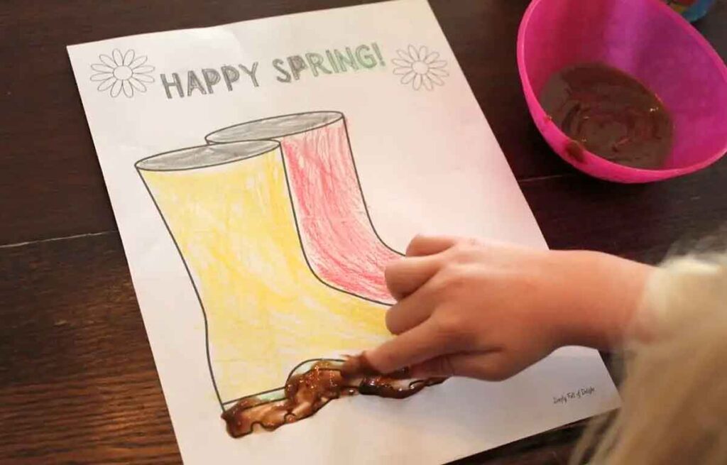 kid's hand putting mud on coloring of boots