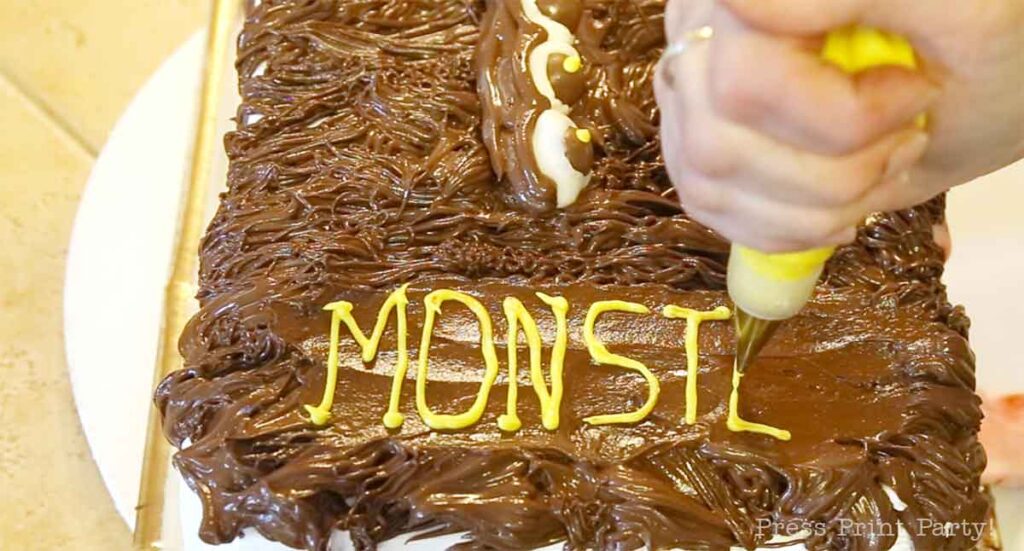 writing the name of the book in yellow writing gel on the monster book of monsters cake - Press Print 