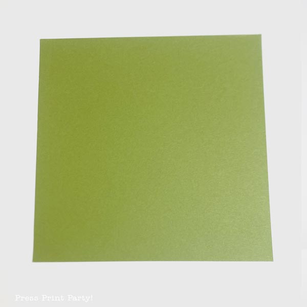A square sheet of green paper, expertly folded into a charming Christmas tree, sits against a plain white background.