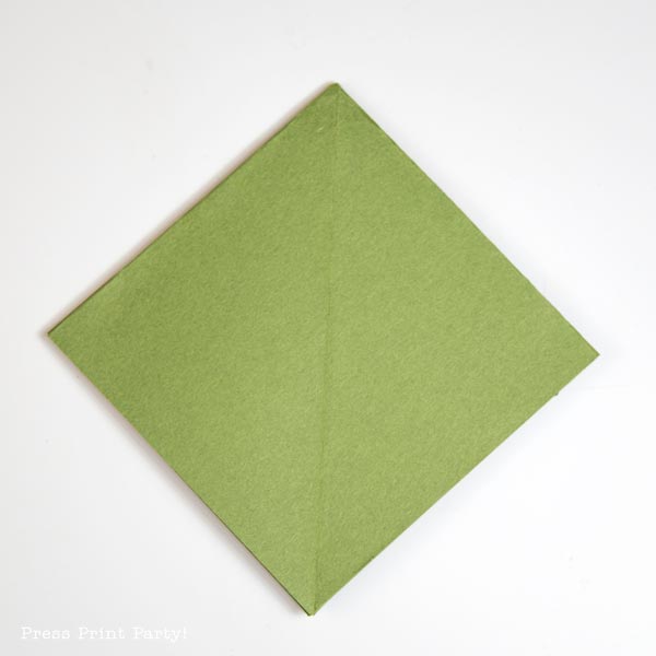 A folded green piece of paper, shaped like a Christmas tree, is artfully positioned in a diamond orientation on a pristine white background.