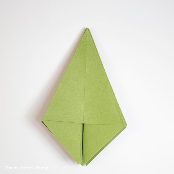 A folded paper creation, crafted from green material, takes the form of a diamond or leaf, subtly evoking the essence of a Christmas tree. It is elegantly displayed on a pristine white background.