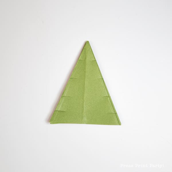 A folded paper Christmas tree, crafted from a green napkin, is elegantly displayed against a crisp white background.