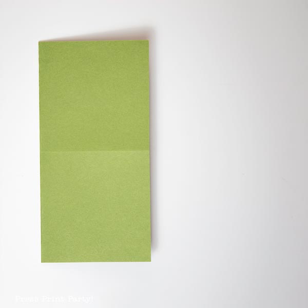 A sheet of green paper is folded in half vertically, resembling a simple Christmas tree when placed on a pristine white background.