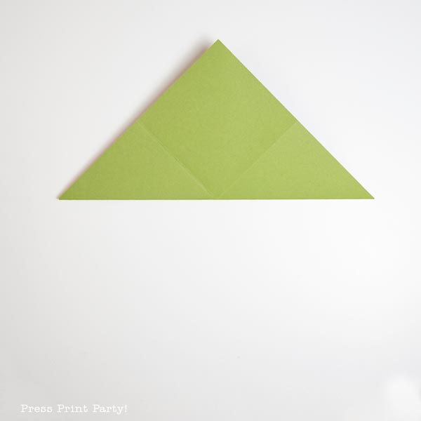A neatly folded green triangular piece of paper resembles a charming Christmas tree against the pristine white background.
