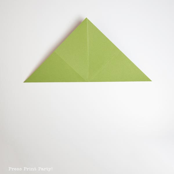 A piece of green paper folded into a triangle shape resembles a minimalist Christmas tree on a white background.