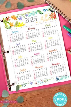 A vibrant 2025 calendar from our Watercolor Calendar Bundle for bullet journals or binders is set on a spiral notebook, decorated with leaves and pens. Each month is elegantly framed with floral borders, providing timeless beauty. A blue 