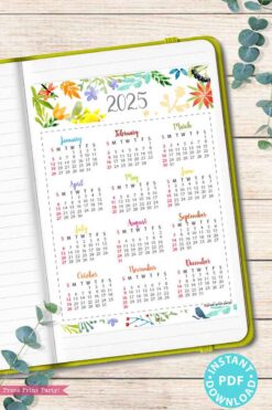 An open notebook showcases a vibrant page from the 2025 Calendar Bundle for Bullet Journals or Binders, Watercolor, featuring a colorful floral design. Alongside it, there's a lively 2025 calendar printable with months displayed alongside week numbers. The decorative elements include a green border and scattered eucalyptus leaves, complemented by a blue 